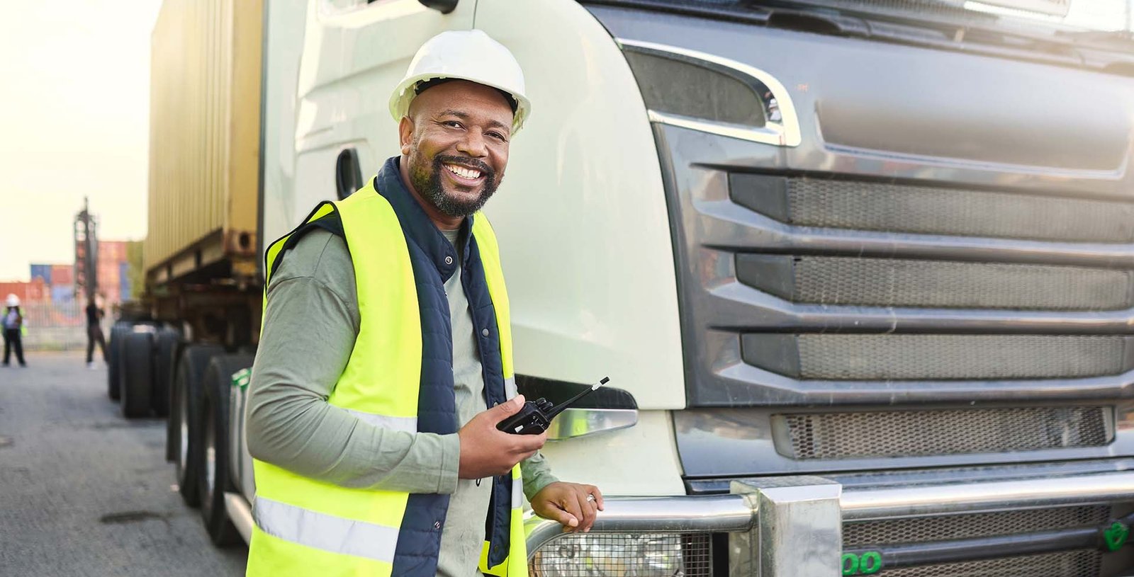 Smiling truck driver with radio beside semi-trailer.